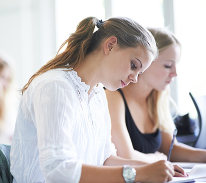 Student taking notes at a classroom desk - Tulane SoPA