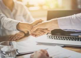 Two business people shaking hands over a desk