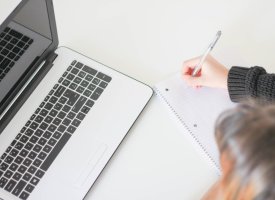 A student taking notes next to a laptop